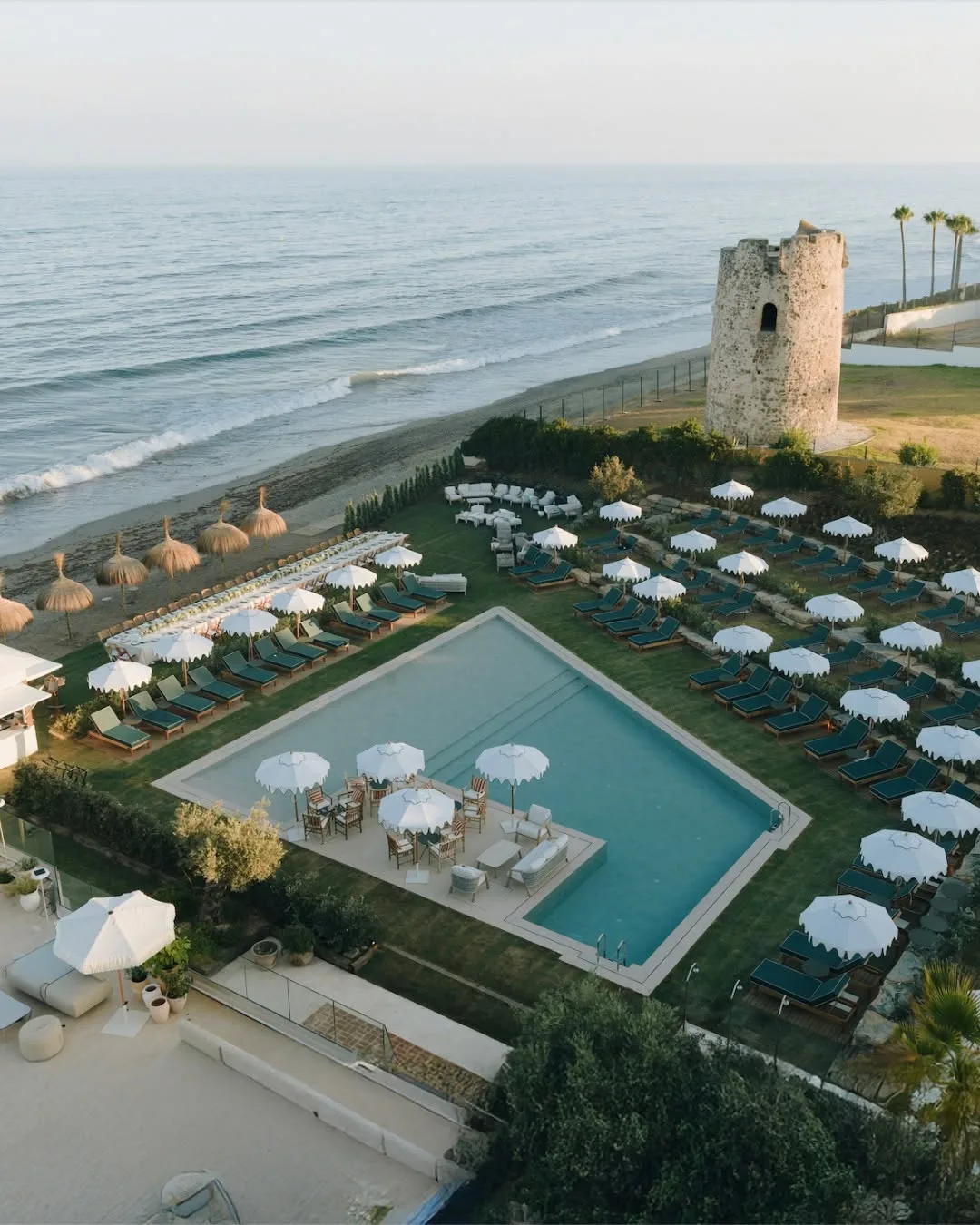 Barbillón from above — pool, sunbeds and the old watchtower by the sea